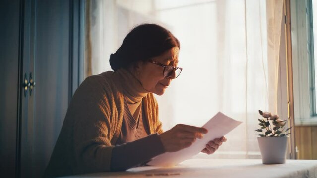 Senior woman reading a letter with bad news and crying, debts and poverty