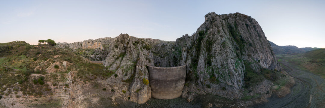 Panoramic view of rugged mountains with the Damn of Montejaque against a clear sky.