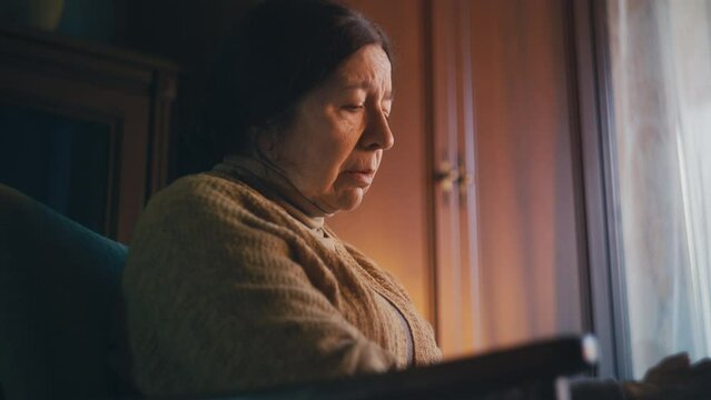 Old woman looking at family photo, missing relatives, loneliness in senior age