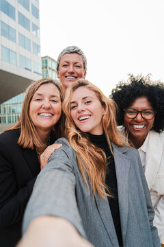 Vertical portrait. Group of real successful business woman smiling and having fun taking a selfie together. Teamwork of entrepreneur females looking at camera. Happy startup ladies laughing at work