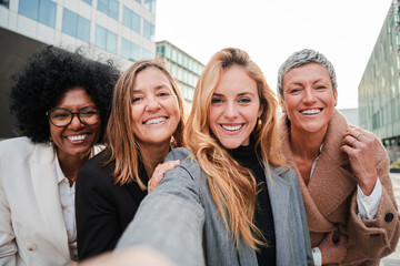 Group of real successful business woman smiling and having fun taking a selfie portrait together. Teamwork of entrepreneur females looking at camera. Happy startup executive ladies laughing at work