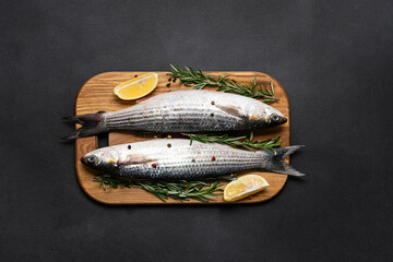 Raw grey mullet fish with spices and herbs in the cooking pan on black stone table top view. Raw fish ready to cook.