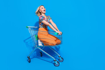 Full length photo of good mood adorable girl riding fast on shopping cart to empty space announcing...