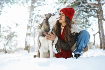 A fluffy husky and his owner play together on a walk in the snowy forest. Walking concept, winter time.