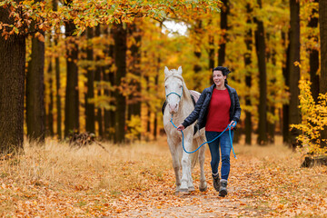 A pretty young woman and a white horse they walk through the woods side by side