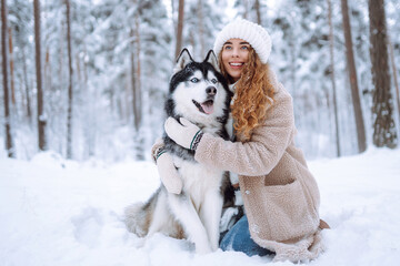Cute woman playing with her dog in the snow. A happy woman and a Siberian husky are walking together in a snowy forest. The concept of holiday, relaxation.