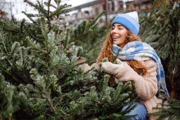 Happy woman buying a Christmas tree. A smiling woman in warm clothes chooses a Christmas tree at the market. Holiday concept.