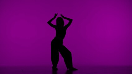 Fototapeta na wymiar In the frame on the purple background in the silhouette. Dances slender, beautiful girl. Demonstrates dance moves in the style of hip hop, lifting hands up. It is feminine, plastic, rhythmic