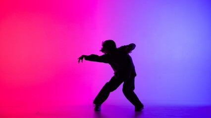 Fototapeta na wymiar In the frame on the purple, pink, gradient background in the silhouette. Dances slim, beautiful girl. Shows dance moves in the style of hip hop, hands to the side. It is feminine, plastic, rhythmic