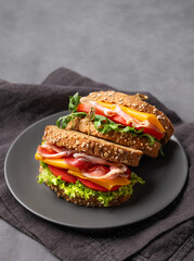 Club sandwich on a plate with a bacon, cheese, tomato and lettuce on a dark background.