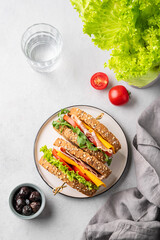 Club sandwich on a plate of bacon, cheese, tomato and lettuce on a light background