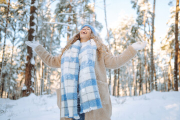 Fototapeta na wymiar Happy woman wearing scarf and hat on snowy winter day outdoors. Young woman having fun with snow on a frosty day. Walking concept.