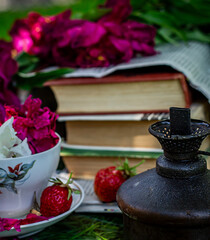 Garden composition, peony petals in a white cup, strawberries and books in the garden