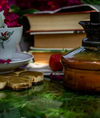 Garden composition, peony petals in a white cup, strawberries and books in the garden