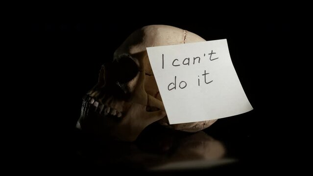 Problem of powerlessness on black. A view of human skull with paper with can not doing it on the black background. A concept of powerlessness time in person life.