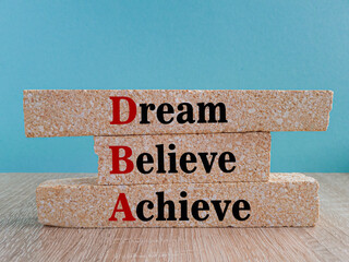Dream Believe Achieve symbol. DBA acronym on brick blocks with letters. Beautiful blue background, wooden table. Concept image of Business Acronym DBA as Dream Believe Achieve
