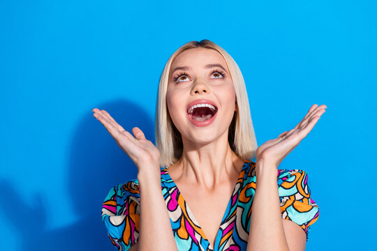 Portrait of overjoyed girl wear stylish shirt look up at promo title empty space catch product isolated on vivid blue color background