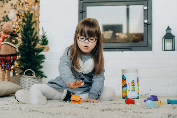 A little girl with Down syndrome plays in the house near the fireplace on Christmas Eve.
