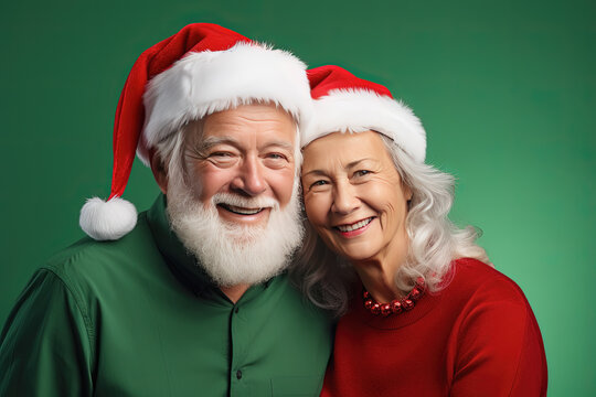 pareja de hombre y mujer mayores llevando gorro de papá noel, sobre fondo verde