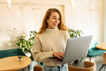 Young woman works with a laptop while sitting in a cafe. Freelancer works online in a modern coffee shop. Concept of technology, freelancing. Lifestyle.