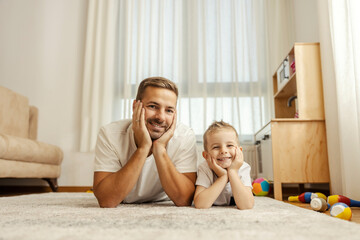 Portrait of a happy father and son lying on the floor at home and smiling at the camera.