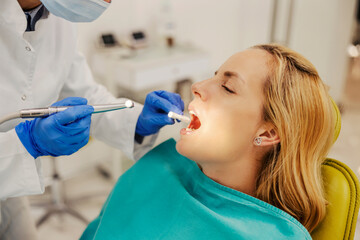 Close up of woman with opened mouth at dentist office during tooth drilling procedure.