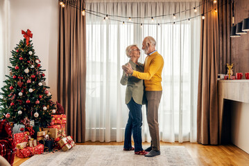 A playful senior couple is dancing at home on christmas and new year.