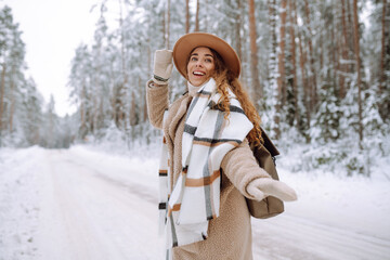 Winter walk. A young woman in winter clothes is having fun in a snowy forest. A beautiful female tourist in a hat enjoys a frosty day in the forest.