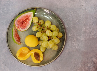 Fruits on a gray plate and on a gray background: figs, white grapes, apricot, selective focus, top view with space for inscription, horizontal orientation. - 686353237