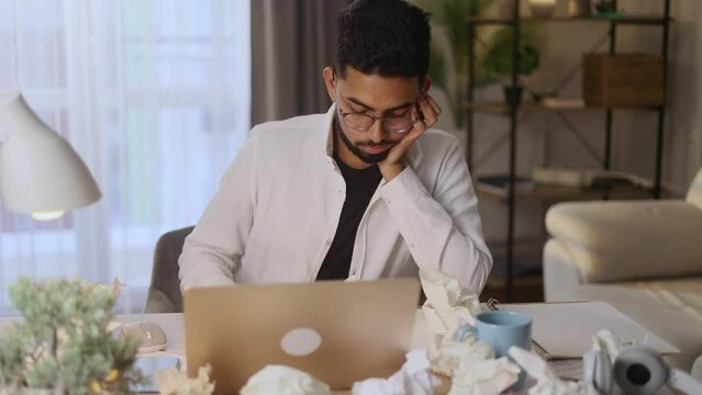 Portrait of exhausted tired young man student or freelancer with failed ideas while take break at home workplace Tired indian male with creative block or lack of inspiration throw away papers indoors	