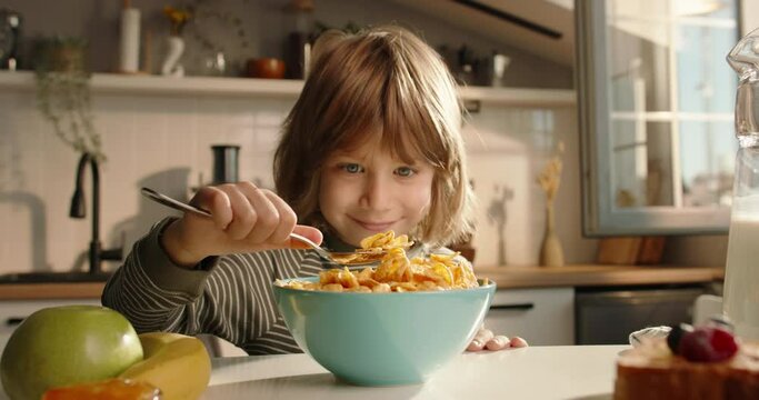 Adorable child eats cereal for breakfast at beautifully decorated table in modern kitchen. Advertising cinematic slow motion. Healthy children's traditional breakfast concept balanced food whole grain