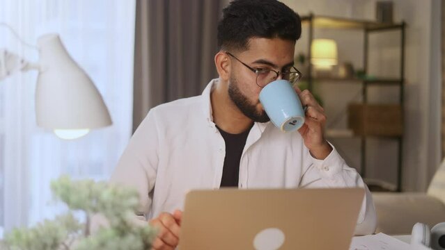 Smiling freelancer having remote work on laptop checking email surfing web and drinking hot coffee or tea indoors Busy young man student having online distance education on computer at home workplace