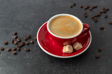 Red white cup of fresh hot coffee with roasted beans and brown sugar pieces closeup on dark grey...