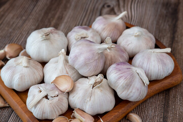 A large head of garlic lies on a wooden plate on a black background.