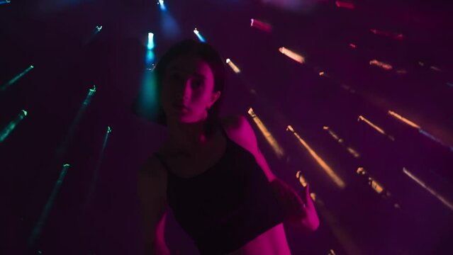In the shot on a dark background with rainbow rays that break through the fog, creating a glare. The girl demonstrates the dance movement in the style of hip hop. She is attractive feminine, rhythmic