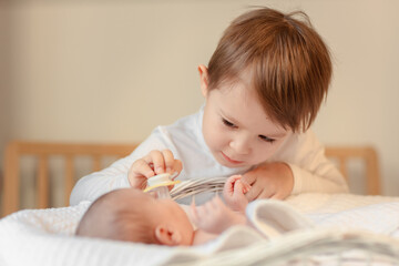 brother and newborn sister, boys giving pacifier to baby, happy family