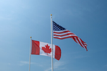 USA and Canadian flags waving left to right against blue sky. Economy, politics concept.