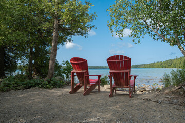 Two bright red wooden muskoka adirondack chairs on the Georgian Bay shore in Brice Peninsula...
