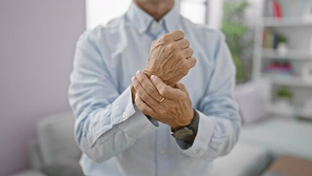 At home, a cool-looking middle age man, in his living room, suffering intense wrist pain, an alarming adult problem, fights hard against this troublesome joint injury.