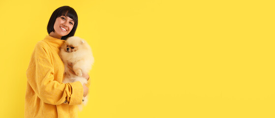 Young Asian woman hugging Pomeranian spitz on yellow background with space for text