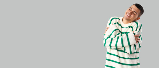 Young man hugging himself on light background with space for text