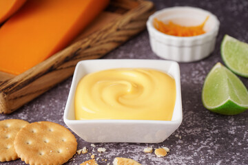 Bowl of tasty cheddar cheese sauce with crackers on black grunge background