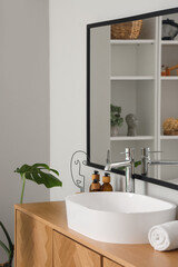 Fototapeta na wymiar White sink with bath accessories on chest of drawers in room