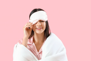 Young woman with sleeping mask and blanket on pink background