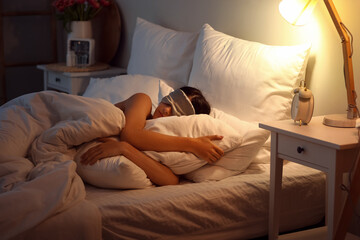 Young woman with mask sleeping in bed at night - obrazy, fototapety, plakaty