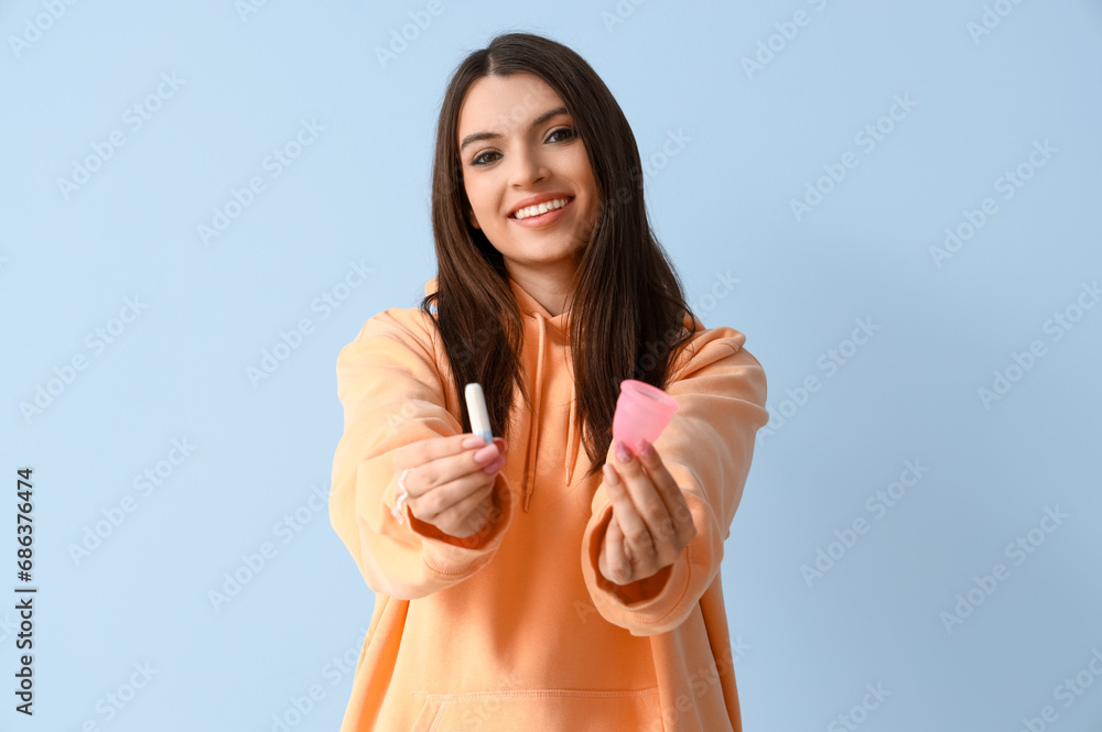 Wall mural Young woman with tampon and menstrual cup on blue background