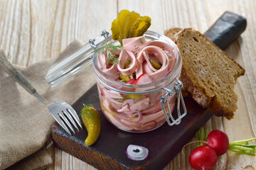 Deftiger bayerischer Wurstsalat mit Fleischwurst im Glas serviert – Hearty Bavarian sausage salad served in a glass jar on an old wooden cutting board 