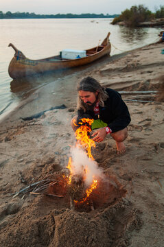 A bearded man builds a fire on a beach along the Mississippi River in the Delta region