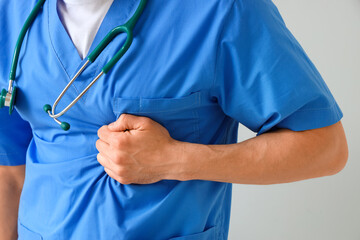 Male doctor having heart attack on light background, closeup