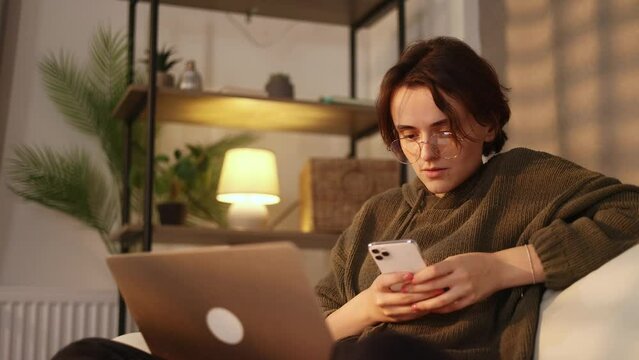 Portrait of creative young freelancer businesswoman have break using social media application on smartphone texting messages receive news check email sitting at couch in the home indoors